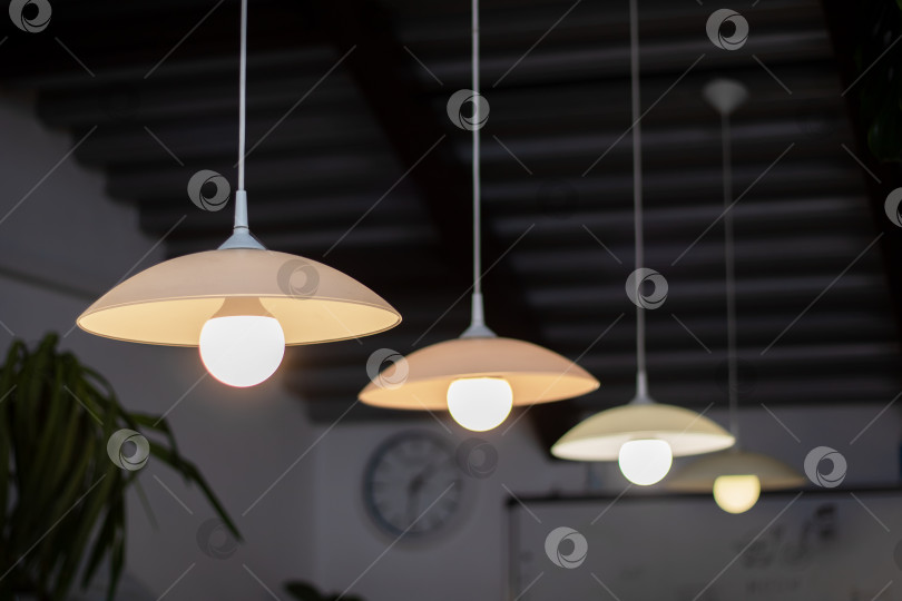Скачать Потолочный светильник с лампами разных оттенков и абажурами, часы на заднем плане фотосток Ozero