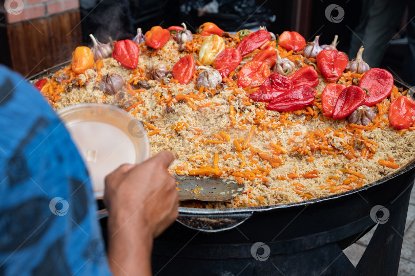 Скачать Повар выкладывает горячий вкусный плов из казана на пластиковую тарелку. Азиатская уличная еда фотосток Ozero