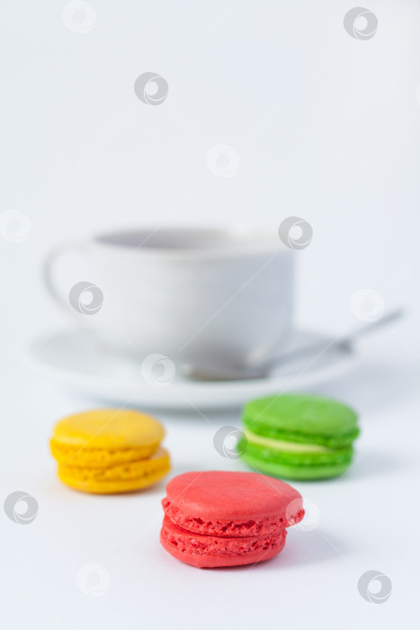 Скачать Традиционные французские разноцветные пирожные макароны на переднем плане и чашка чая на блюдце в размытом виде на белом фоне фотосток Ozero