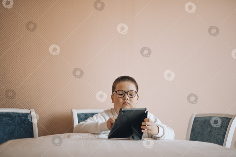 Скачать мальчик в очках сосредоточенно смотрит на планшет, что наводит на мысль о начале цифрового исследования фотосток Ozero
