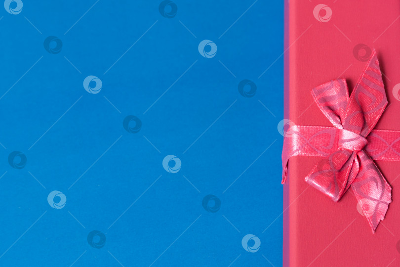 Скачать Вид сверху на красную подарочную коробку в правом углу с лентой и бантом на синем фоне с пробелом для копирования фотосток Ozero