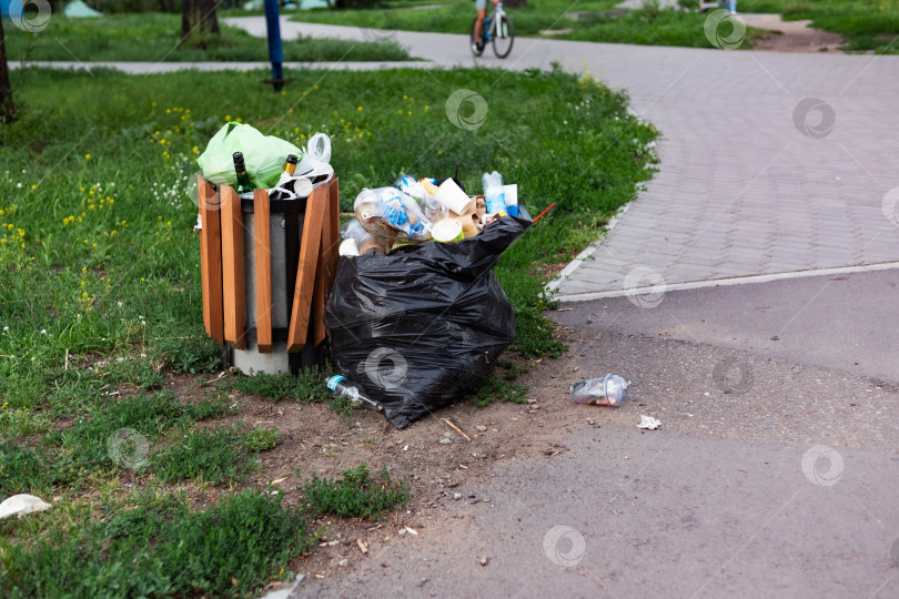 Скачать Переполненный зеленый мусорный бак в Суррей-парке примыкает к тропинке Темзы. фотосток Ozero