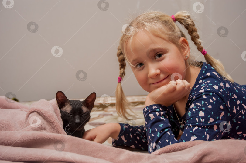 Скачать 8-летняя девочка лежит в постели с котом-сфинксом фотосток Ozero