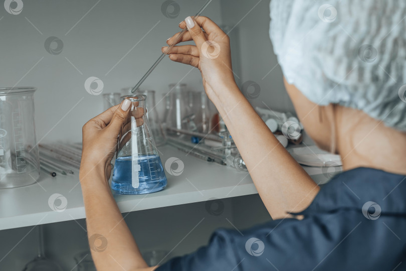 Скачать Женщина-ученый в шапочке со стеклянной трубкой, наполненной синей химической жидкостью для исследований и анализа в лаборатории. фотосток Ozero