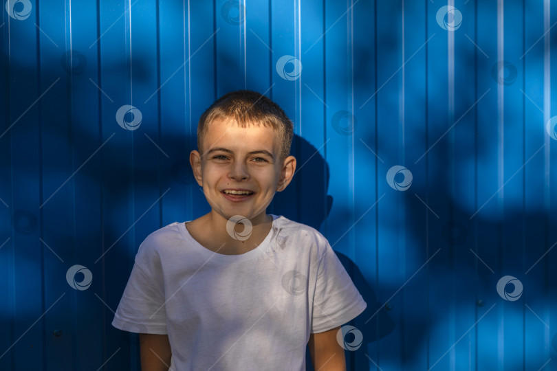 Скачать Маленький счастливый мальчик 10 лет в белой повседневной футболке, улыбающийся на простом синем фоне фотосток Ozero