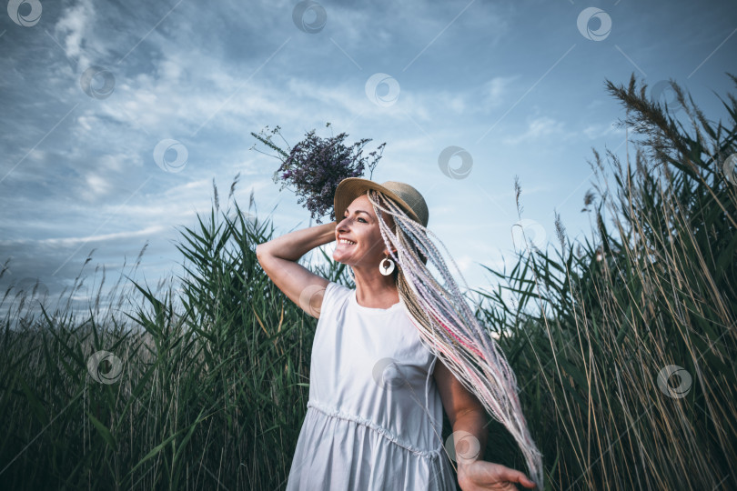 Скачать девушка с яркими косичками в соломенной шляпе, держащая букет цветов, ветер на природе фотосток Ozero