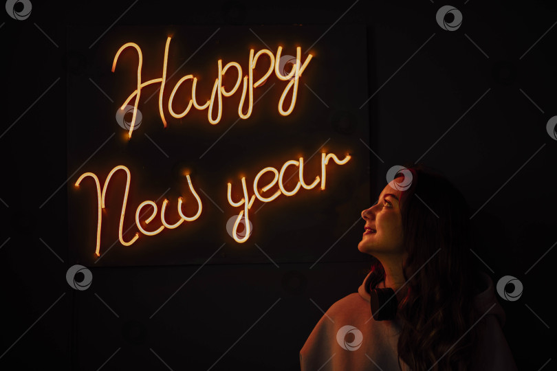Скачать профиль красивой девушки в наушниках ночью на фоне светящейся оранжевой надписи New Year на черном фоне. фотосток Ozero