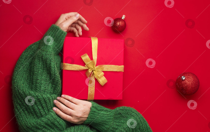 Скачать дама в зеленом свитере обнимает красную подарочную коробку с золотой лентой, подарок ее мечты на красном фоне. фотосток Ozero