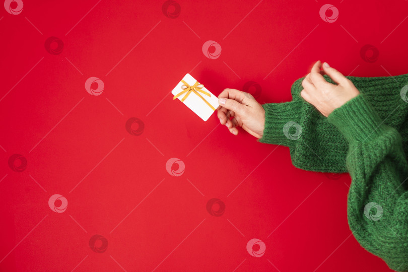 Скачать Концепция рождественских покупок. Руки в зеленом свитере с бонусной картой лежат ровно. Баннер на красном фоне фотосток Ozero