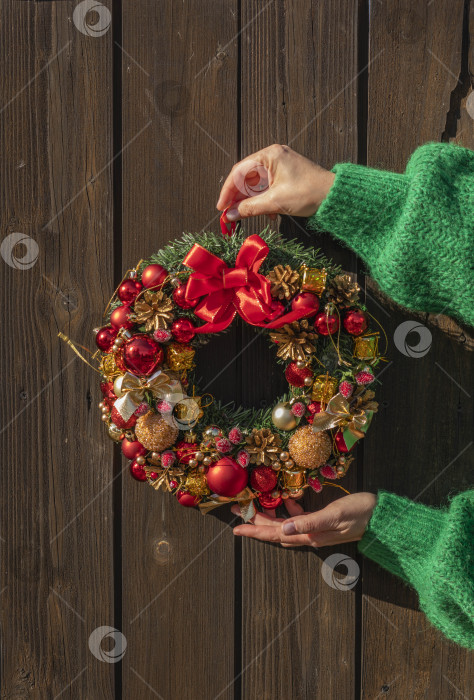 Скачать Женские руки в зеленом свитере развешивают рождественский еловый венок. Канун Рождества и украшение. Празднование Нового года. фотосток Ozero