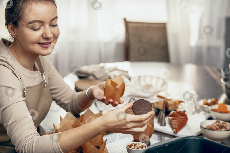 Скачать Молодая женщина упаковывает кексы в форму для выпечки. концепция доставки еды. Подарок на день рождения. небольшой бизнес. шеф-повар пекарни выпекает пирожные и торты на кухне, копировальное помещение фотосток Ozero