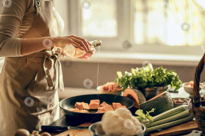 Скачать Руки молодой женщины выкладывают тыкву на сковороду для запекания на кухне. Концепция здорового питания фотосток Ozero