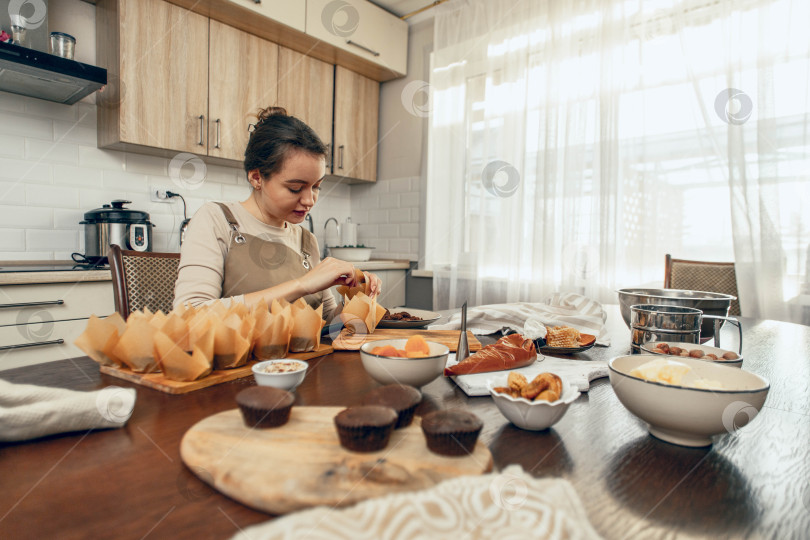 Скачать Молодая женщина упаковывает кексы в форму для выпечки. концепция доставки еды. Подарок на день рождения. малый бизнес. шеф-повар пекарни выпекает пирожные и торты на кухне, копировальное помещение фотосток Ozero