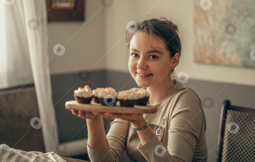Скачать молодая женщина показывает кексы, которые она держит в руке. украшение кремом. Шеф-повар пекарни выпекает кексы на кухне фотосток Ozero