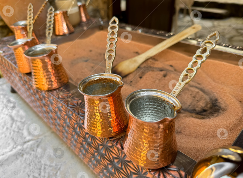 Скачать Традиционный кофе по-турецки в медных турках с длинными ручками на подносе с песком. Приготовление настоящего кофе крупным планом с тщательным отбором. фотосток Ozero