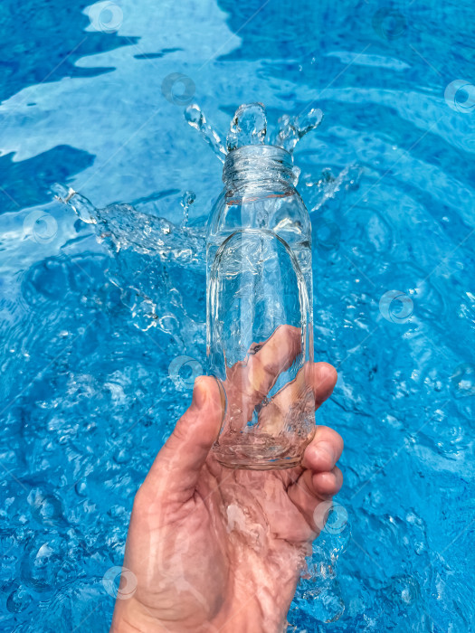 Скачать Рука, выплескивающая воду из прозрачной стеклянной бутылки в голубой бассейн, динамичный стоп-кадр. Концепция чистой воды. фотосток Ozero