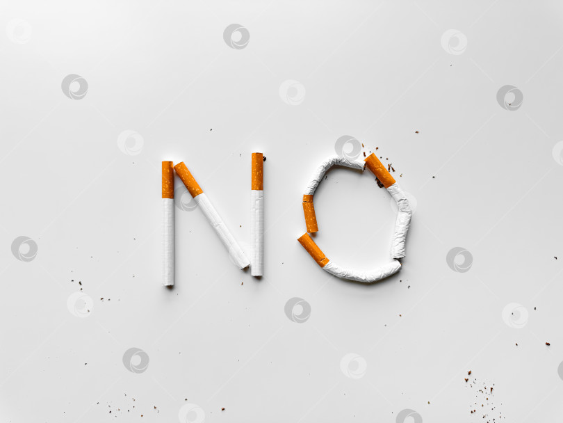 Скачать Надпись "НЕТ", выполненная из сломанных сигарет на белом фоне, является призывом к борьбе с курением. Вид сверху с пространством для копирования, концепция отказа от курения. День без табака фотосток Ozero