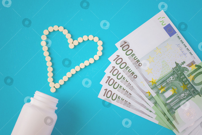 Скачать Желтые таблетки выложены в форме сердца, белая баночка и банкнота в сто евро на синем фоне (концепция, плоское расположение) фотосток Ozero