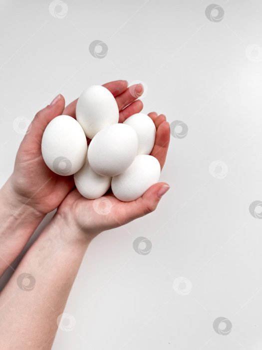 Скачать Руки, сжимающие связку белых яиц на бледном фоне, - символ заботы, питания и новых начинаний. Для кулинарных сайтов, блогов рецептов и руководств по питанию. фотосток Ozero
