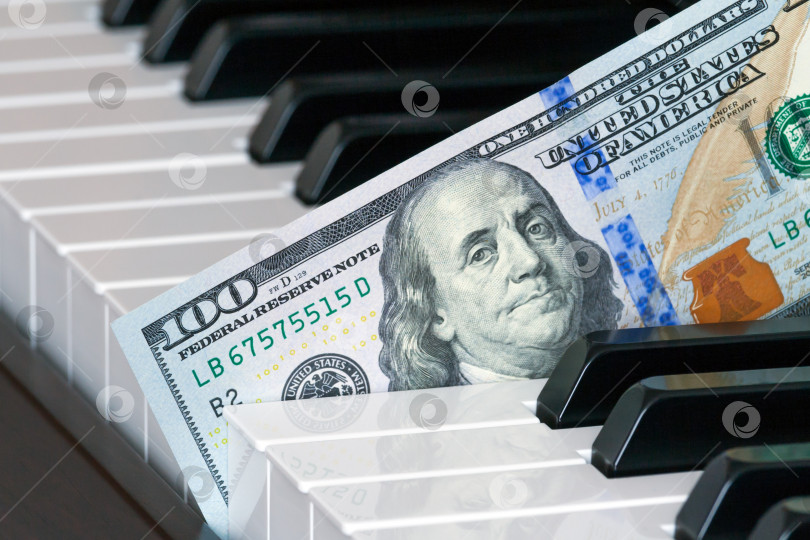 Скачать Вид фрагмента стодолларовой банкноты нового образца, вставленного в клавиши пианино (концепция) фотосток Ozero