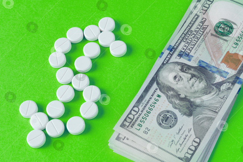 Скачать Вид сверху на белые таблетки, разложенные в форме символа доллара, и кучку банкнот рядом на зеленом фоне (концепция, плоское расположение) фотосток Ozero