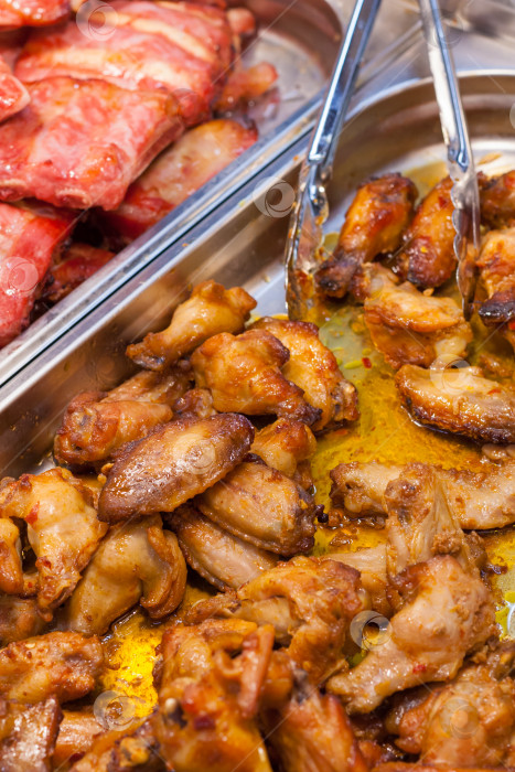 Скачать Приготовленные куриные крылышки с соусом и кухонными щипцами на прилавке супермаркета фотосток Ozero
