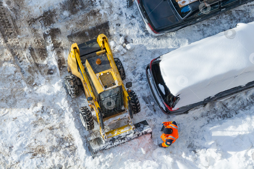 Скачать Снегоуборочная машина и рабочий в оранжевой униформе чистят дорогу. Вид сверху фотосток Ozero