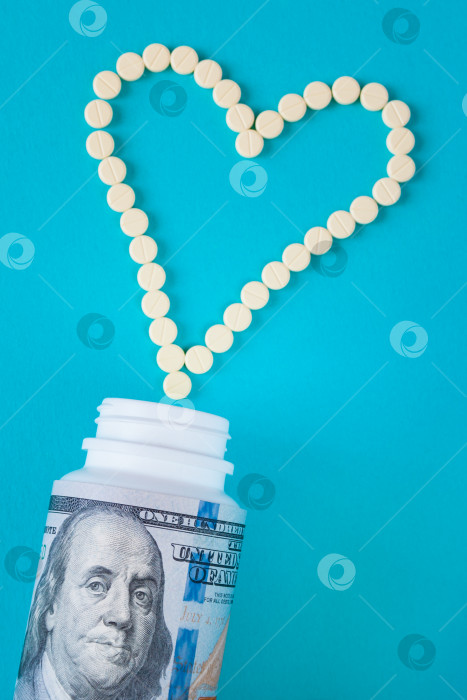 Скачать Желтые таблетки выложены в форме сердца. Белая банка завернута в стодолларовую банкноту на синем фоне (концепция, плоское расположение) фотосток Ozero