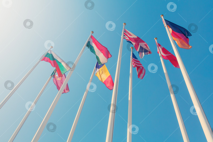 Скачать Вид снизу на флаги разных стран мира на фоне солнечного света в ясном голубом небе (тонированный) фотосток Ozero
