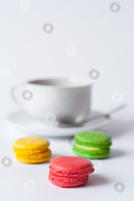 Скачать Традиционные французские разноцветные пирожные макароны на переднем плане и чашка чая на блюдце в размытом виде на белом фоне фотосток Ozero