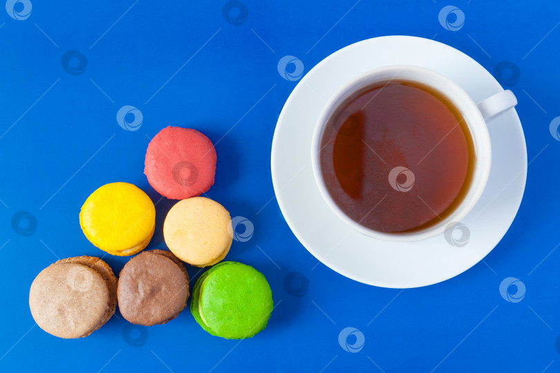 Скачать Вид сверху на французские разноцветные пирожные макароны и чашку чая на блюдце на синем фоне (плоская выкладка) фотосток Ozero