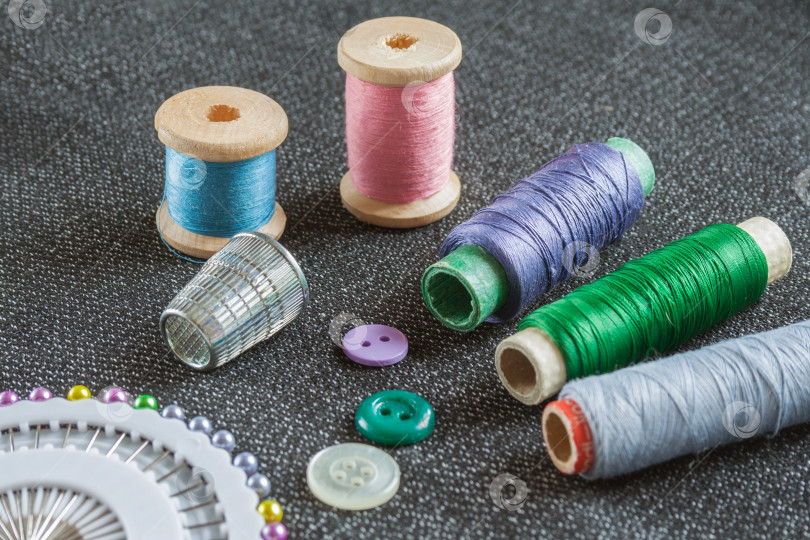 Скачать Швейные принадлежности: катушки с нитками, иголки, наперсток, пуговицы на фактурной поверхности ткани фотосток Ozero