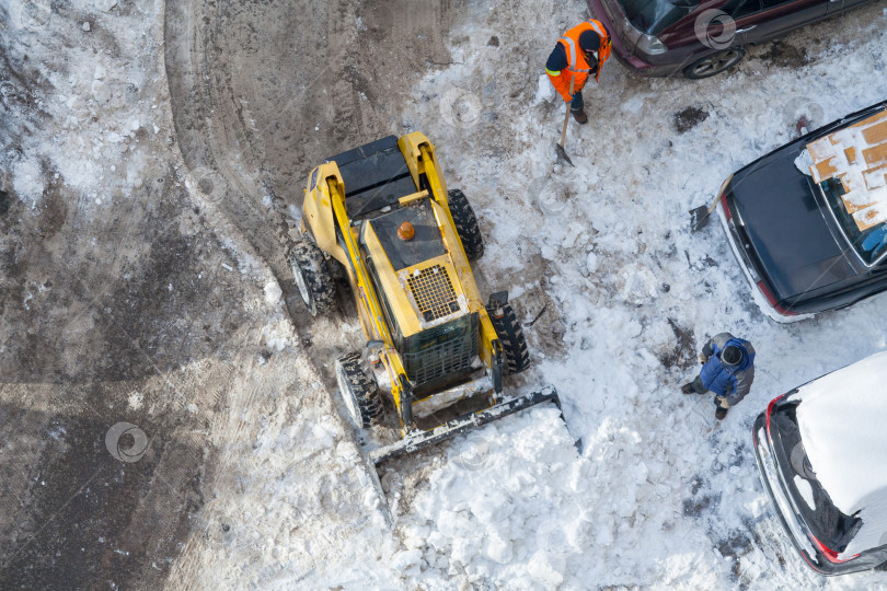 Скачать Вид сверху на снегоуборочную машину, чистящую дорогу, и рабочего в оранжевой униформе фотосток Ozero