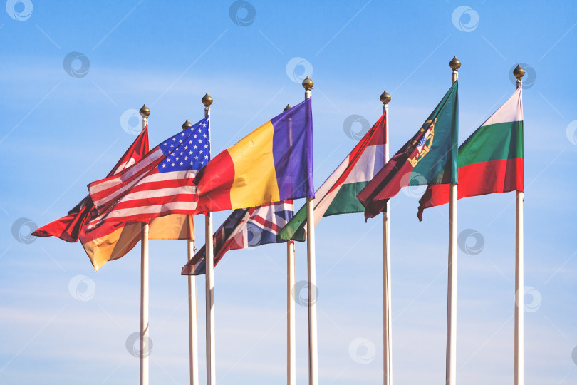 Скачать Флаги разных стран развеваются на ветру на фоне голубого неба с облаками фотосток Ozero