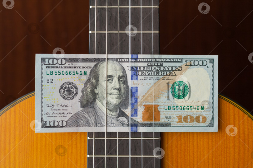Скачать Стодолларовые купюры, вложенные между струнами акустической гитары. Концепция фотосток Ozero