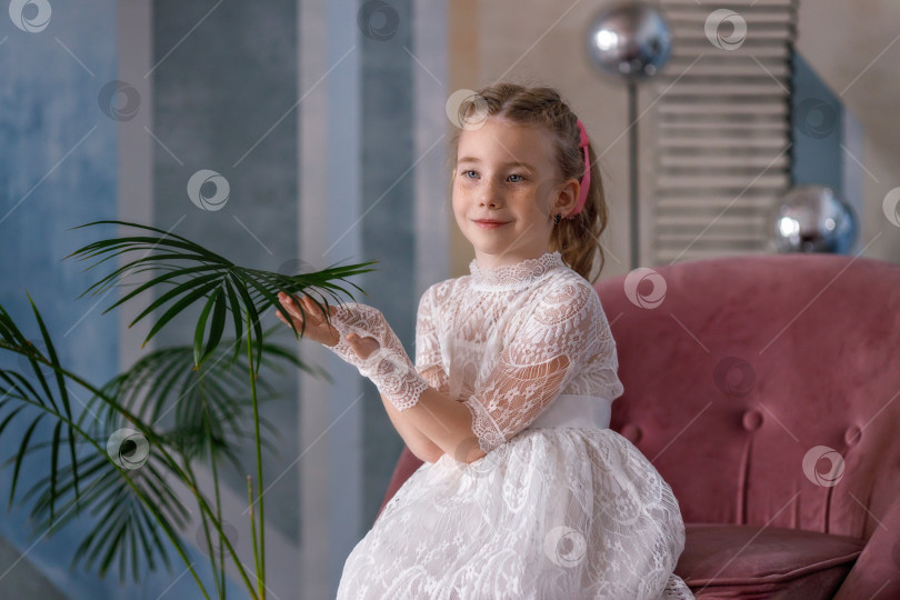 Скачать Симпатичная маленькая девочка-карапуз в белом праздничном платье сидит возле пальмы. Детство фотосток Ozero
