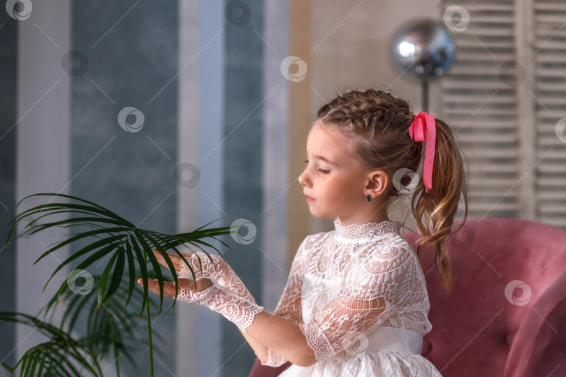 Скачать Симпатичная маленькая девочка-карапуз в белом праздничном платье сидит возле пальмы. Детство фотосток Ozero