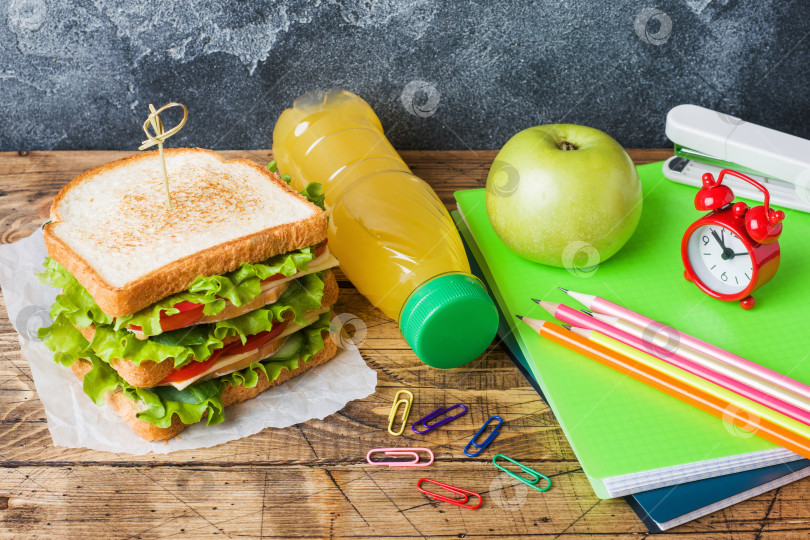 Скачать Полезный обед для школы с бутербродом, свежим яблоком и апельсиновым соком. Разноцветные школьные принадлежности в ассортименте. Место для копирования. фотосток Ozero
