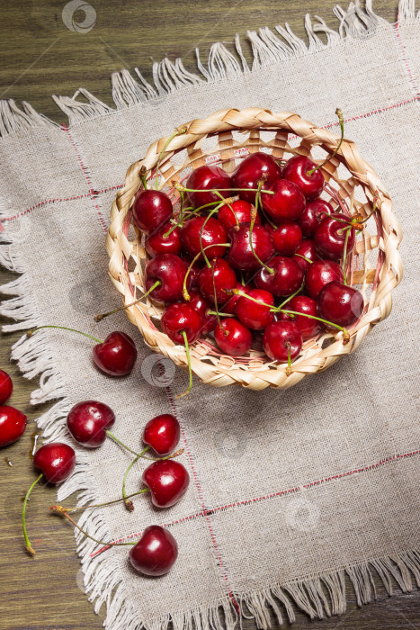 Скачать Спелые вишни в соломенной корзинке на деревянном столе. фотосток Ozero