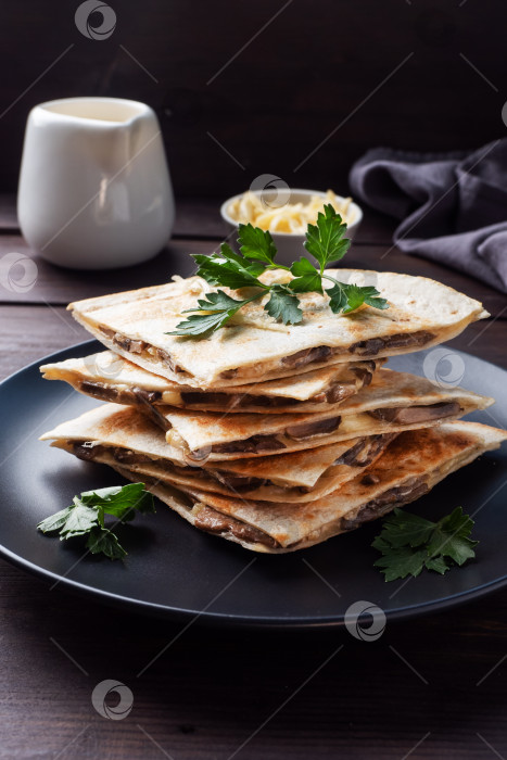 Скачать Кусочки кесадильи с грибами, сметаной и сыром на тарелке, украшенной листьями петрушки. Деревянный фон крупным планом. фотосток Ozero