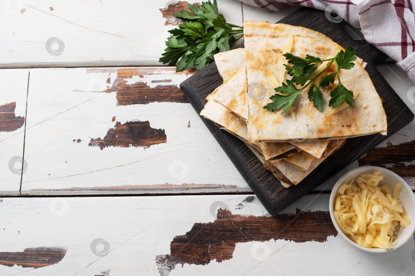 Скачать Кусочки кесадильи с грибами, сметаной и сыром на деревянной подставке с листьями петрушки. Деревянный фон копирует пространство. фотосток Ozero