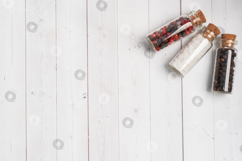 Скачать Специи - черный и красный перец и соль - в стеклянных колбах на белом деревянном фоне с объемным рисунком. фотосток Ozero