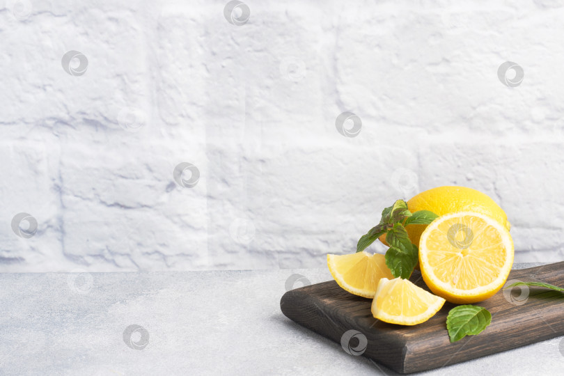 Скачать Целые и нарезанные сочные желтые лимоны с листьями свежей мяты на деревянной подставке. Скопируйте пробел. фотосток Ozero