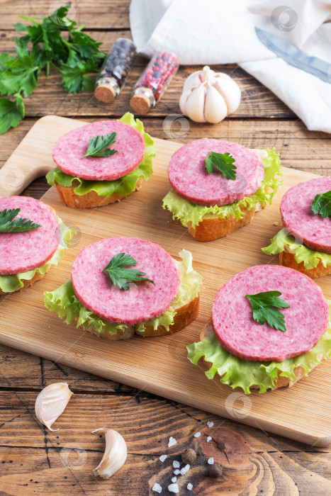Скачать Бутерброды с листьями салата и нарезанной колбасой салями на деревянной доске. фотосток Ozero
